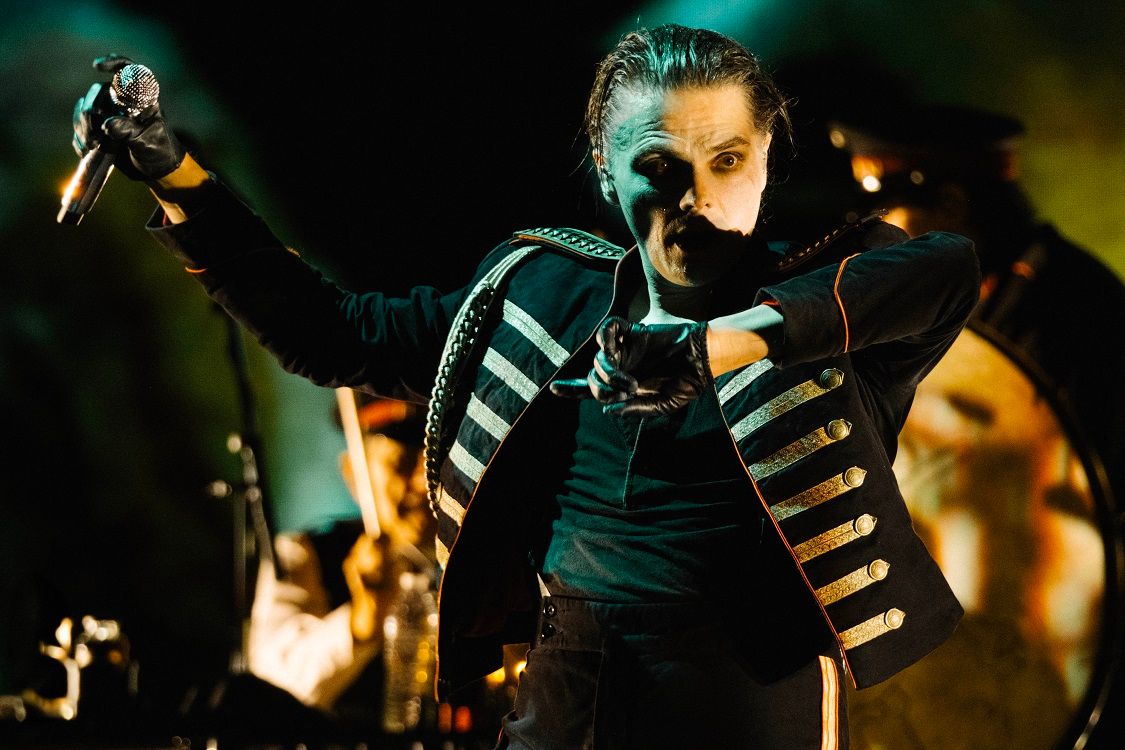 Dramatic concert performance with musicians in black outfits playing on stage with dramatic lighting effects.