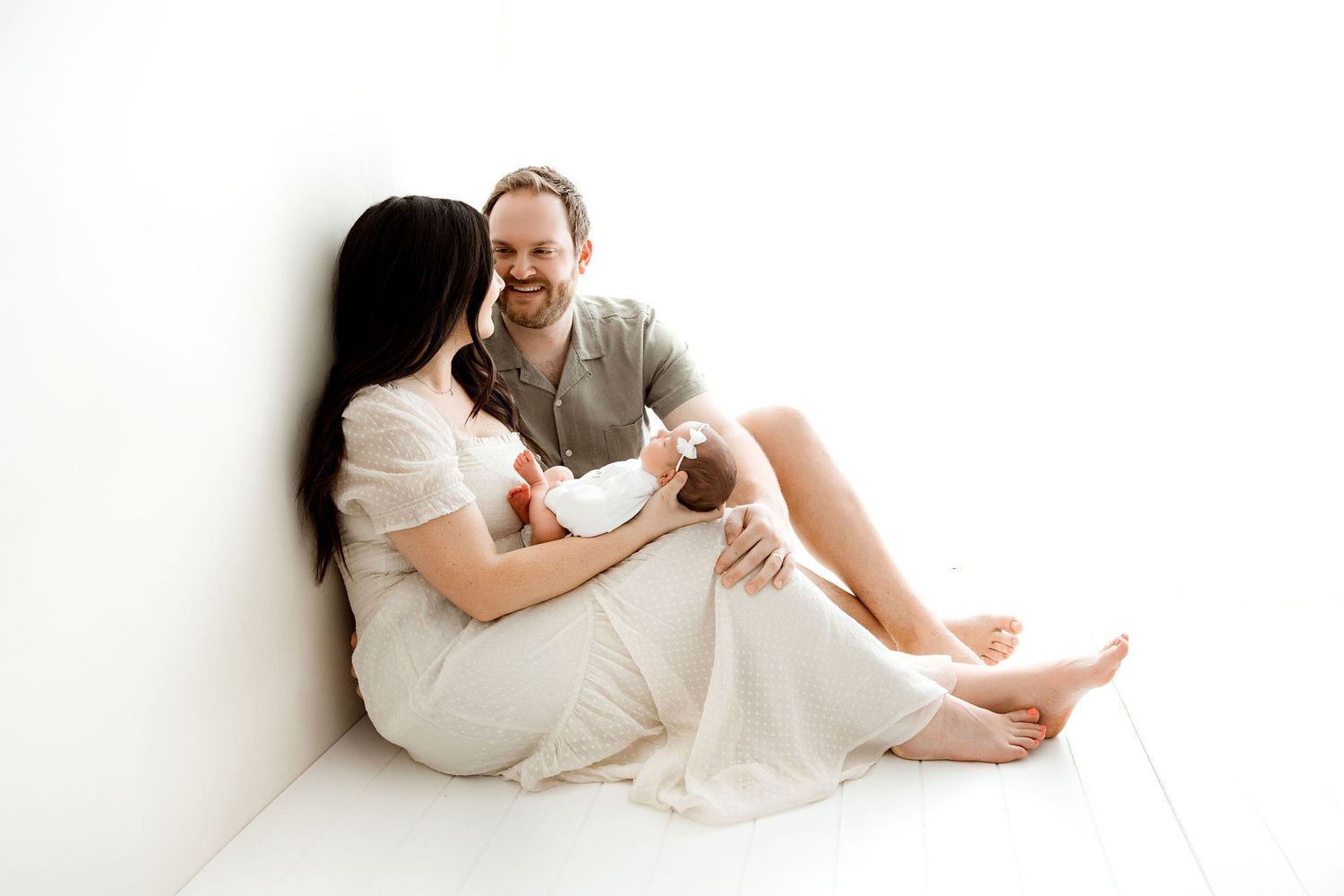 Family with a newborn baby girl sitting on a white floor by the window