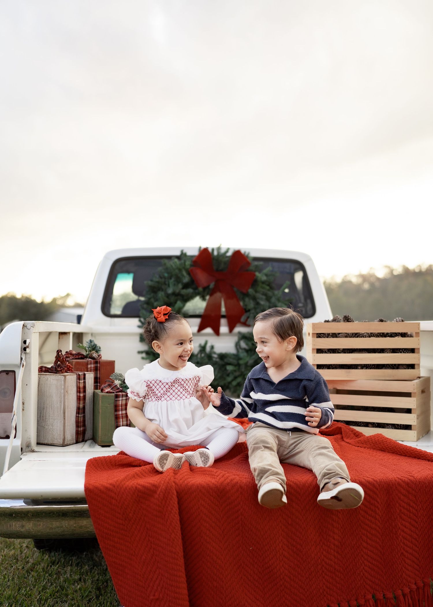 Family enjoying a festive Texas farm Christmas mini session, sitting on the bed of an old red Ford truck decorated with holiday greenery.