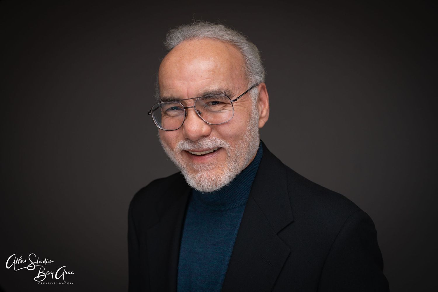 Professional portrait of older person wearing glasses and black turtleneck against dark background.