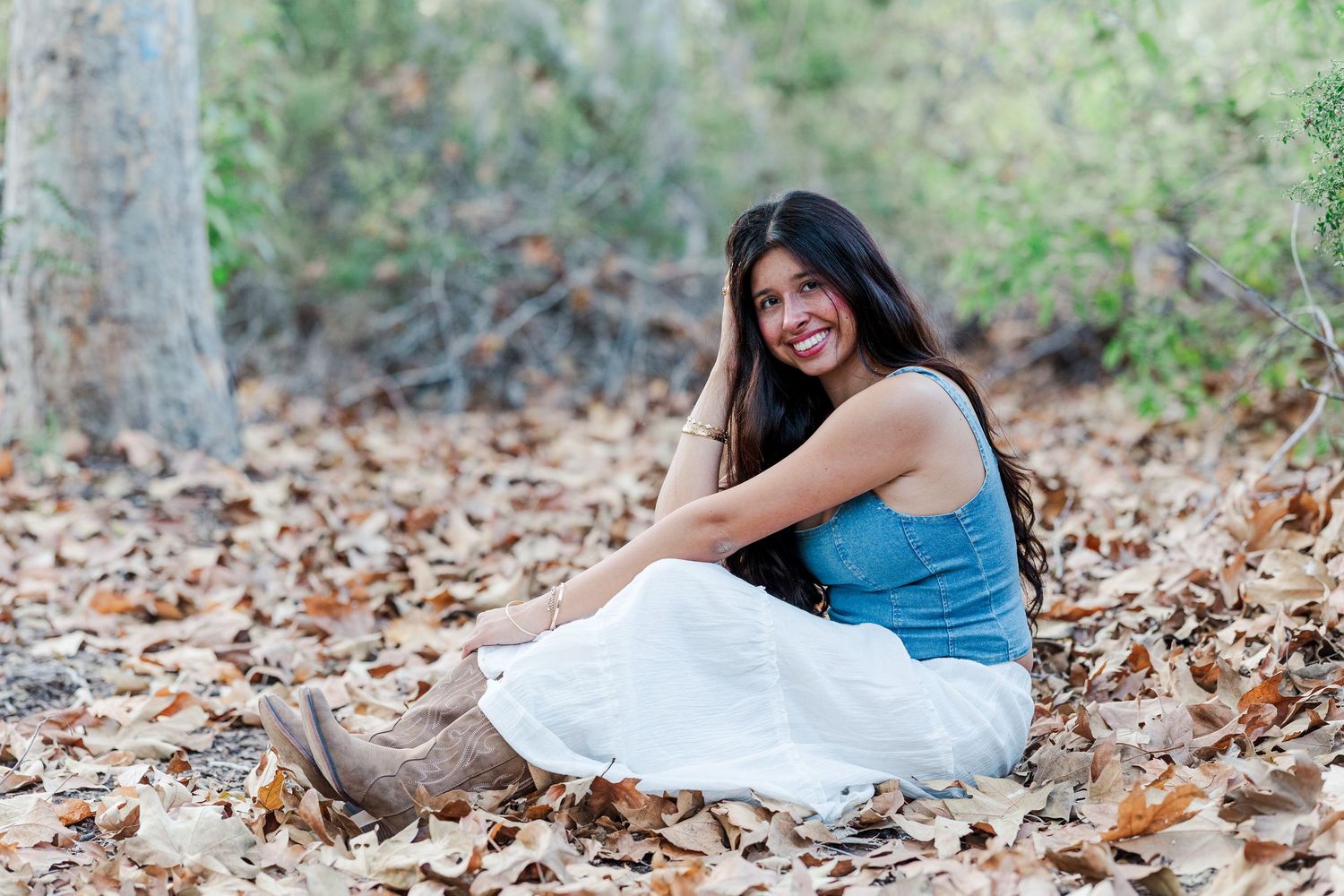 Someone in a blue top lies among autumn leaves while reading a book in a relaxed outdoor setting.
