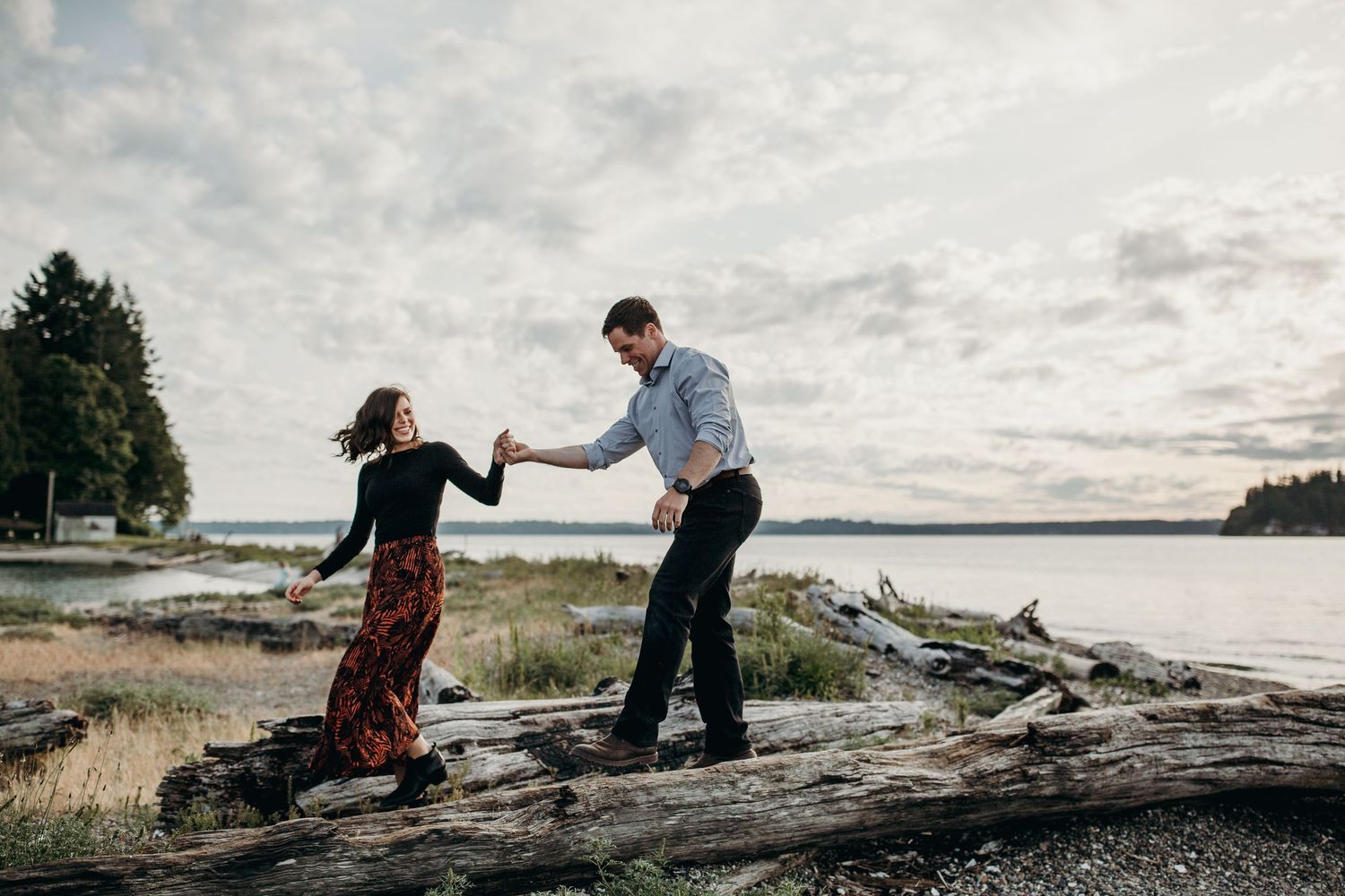 Two people dance together on a rocky beach under cloudy grey skies in a candid moment.