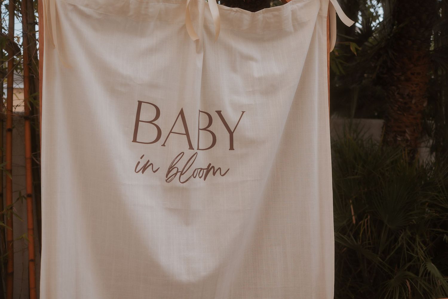 A white cloth banner with 'BABY in bloom' text hangs against a blurred outdoor background.