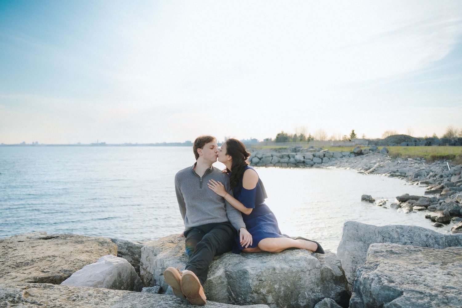 A couple shares an intimate moment while sitting on coastal rocks near the ocean.