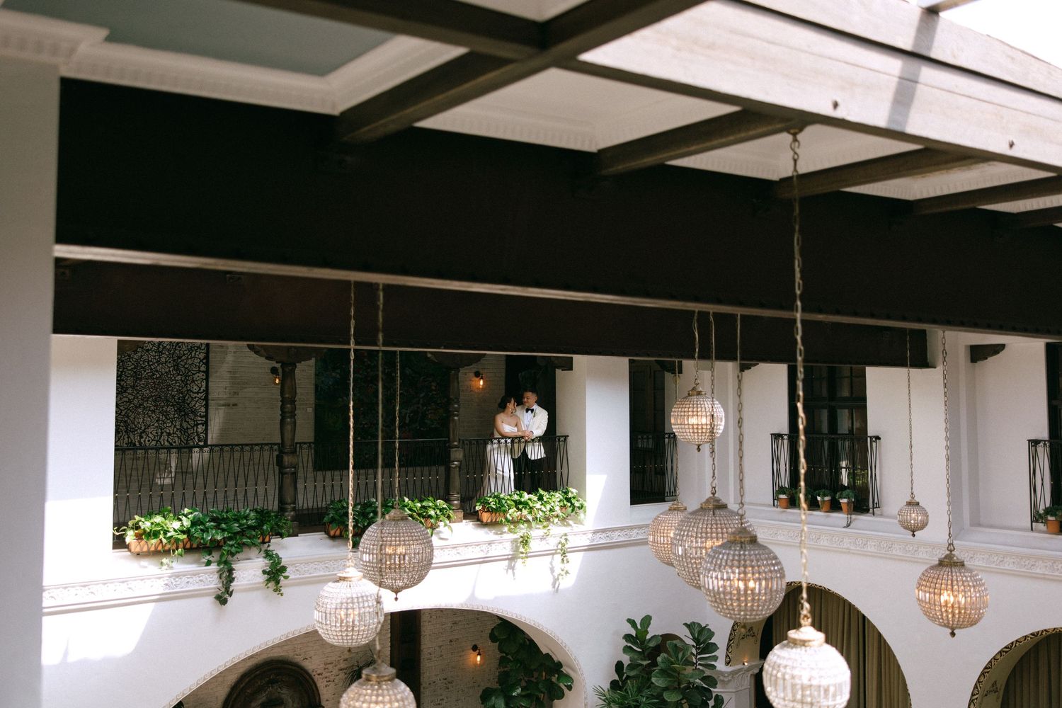 Elegant hotel atrium with hanging crystal globe chandeliers and a person standing on the upper balcony.