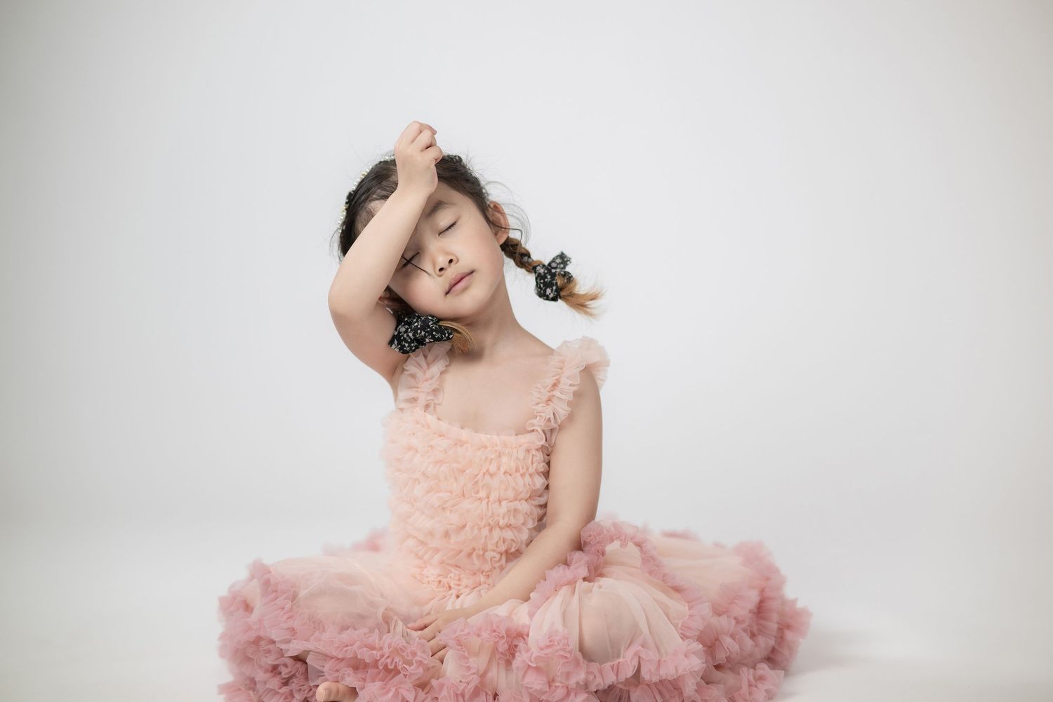 A young dancer in a frilly pink tutu dress sits gracefully against a white background.