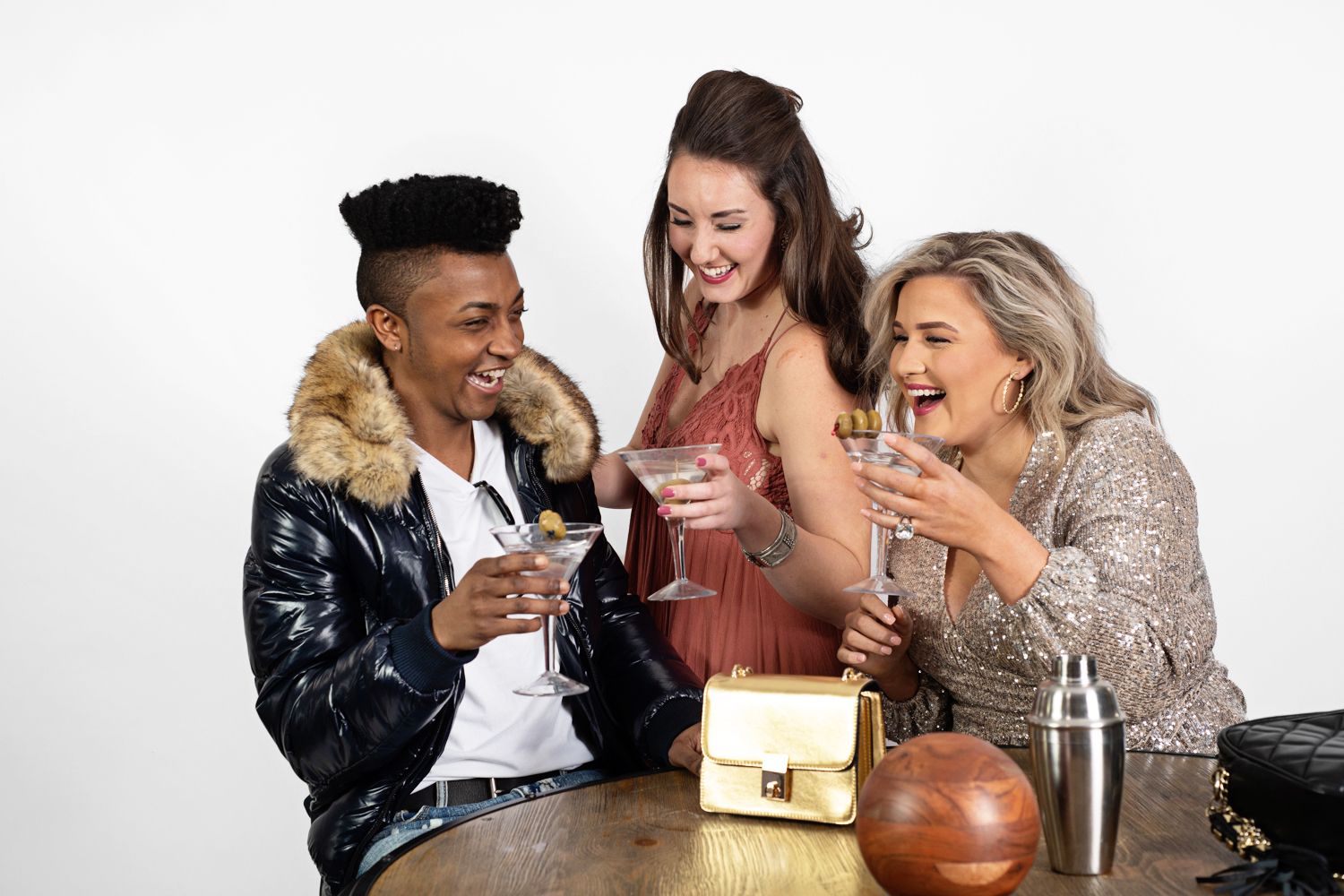 Three friends laughing and socializing while having drinks around a table.
