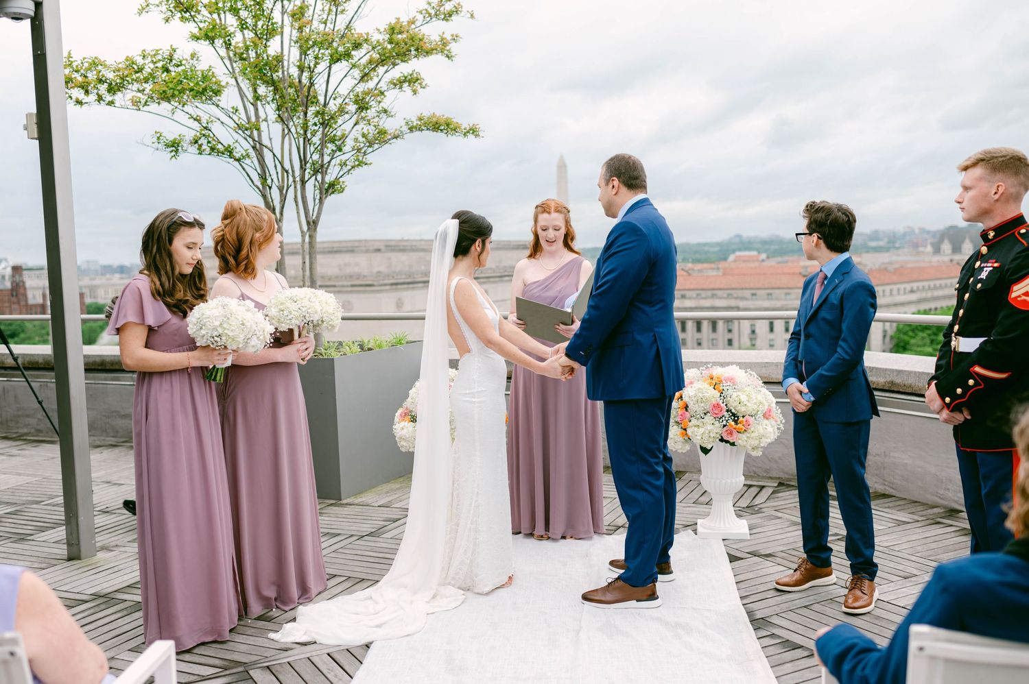 Rooftop wedding ceremony with city skyline backdrop and wedding party in formal attire.