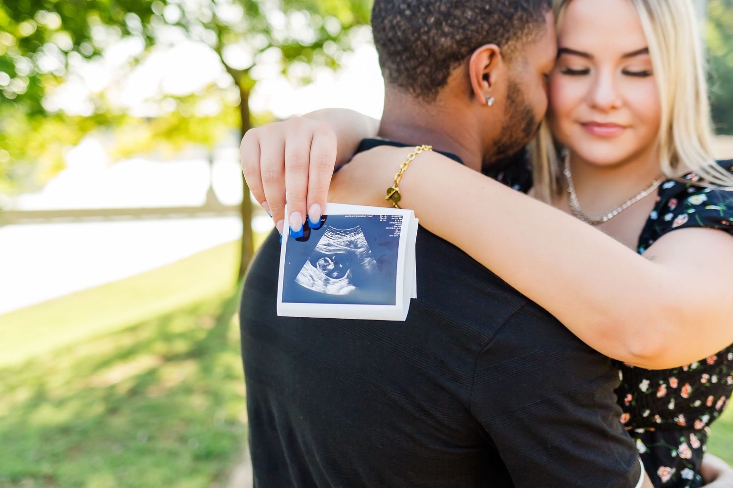 Couple holding ultrasound photos during outdoor pregnancy announcement photoshoot.