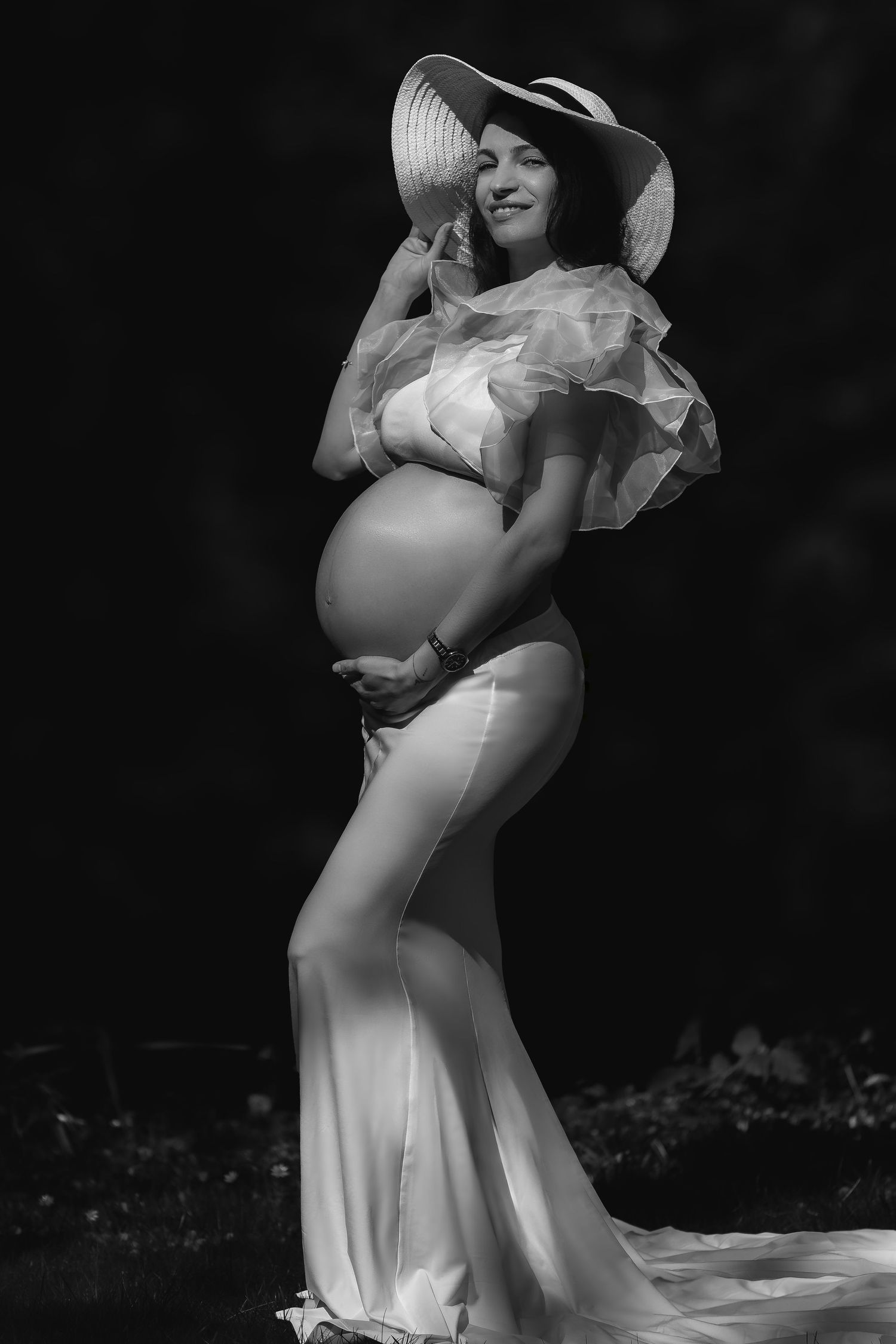 Black and white maternity photoshoot featuring elegant poses in flowing white dresses and sun hats.