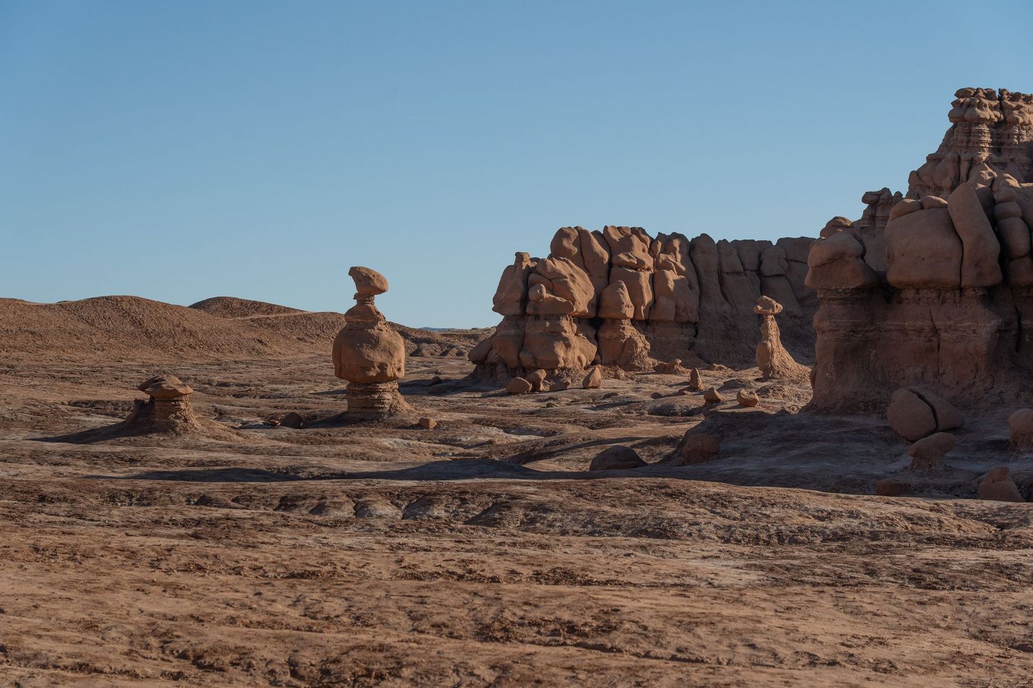 Unique rock formations and hoodoos stand against a clear blue sky in Goblin Valley State Park, Utah.