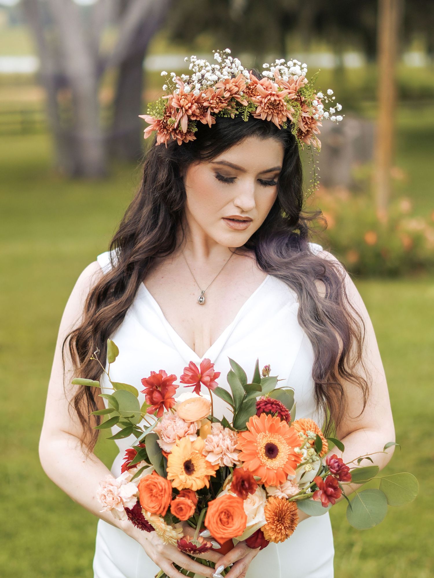 Bride with coral flower crown holds matching bouquet in garden setting.