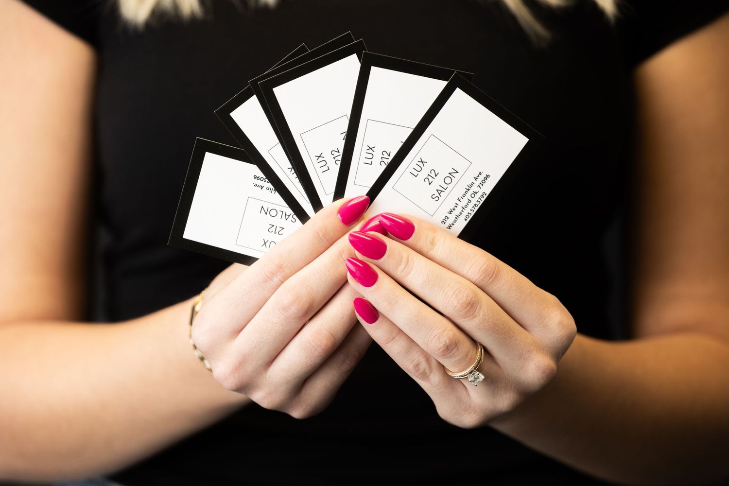Hands with red nail polish holding a fan of white business cards against a black background.