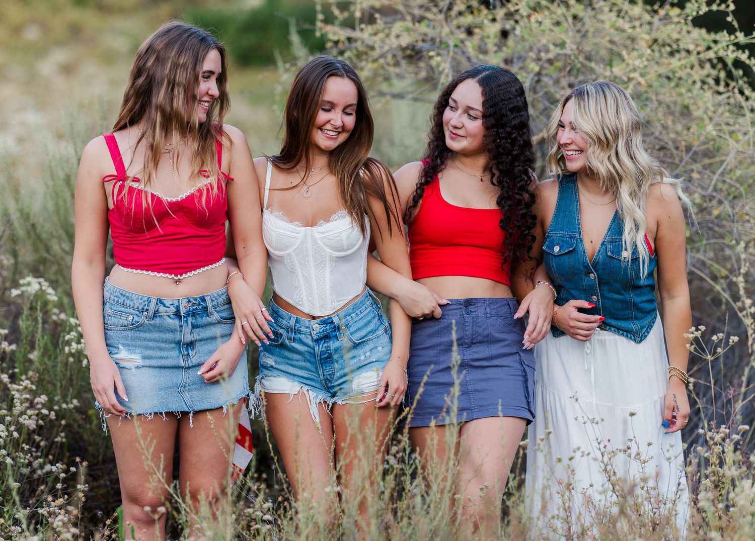 Four friends in summer outfits pose together in a wildflower field.