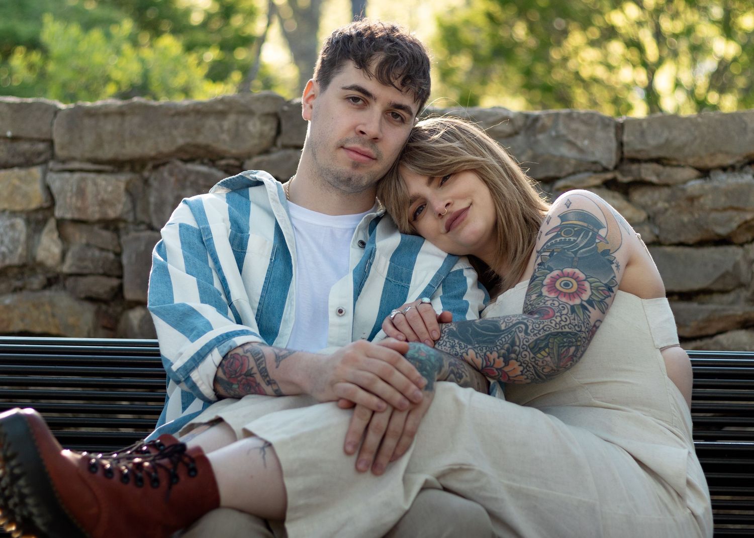 A romantic couple lounges together on a bench against a stone wall backdrop.