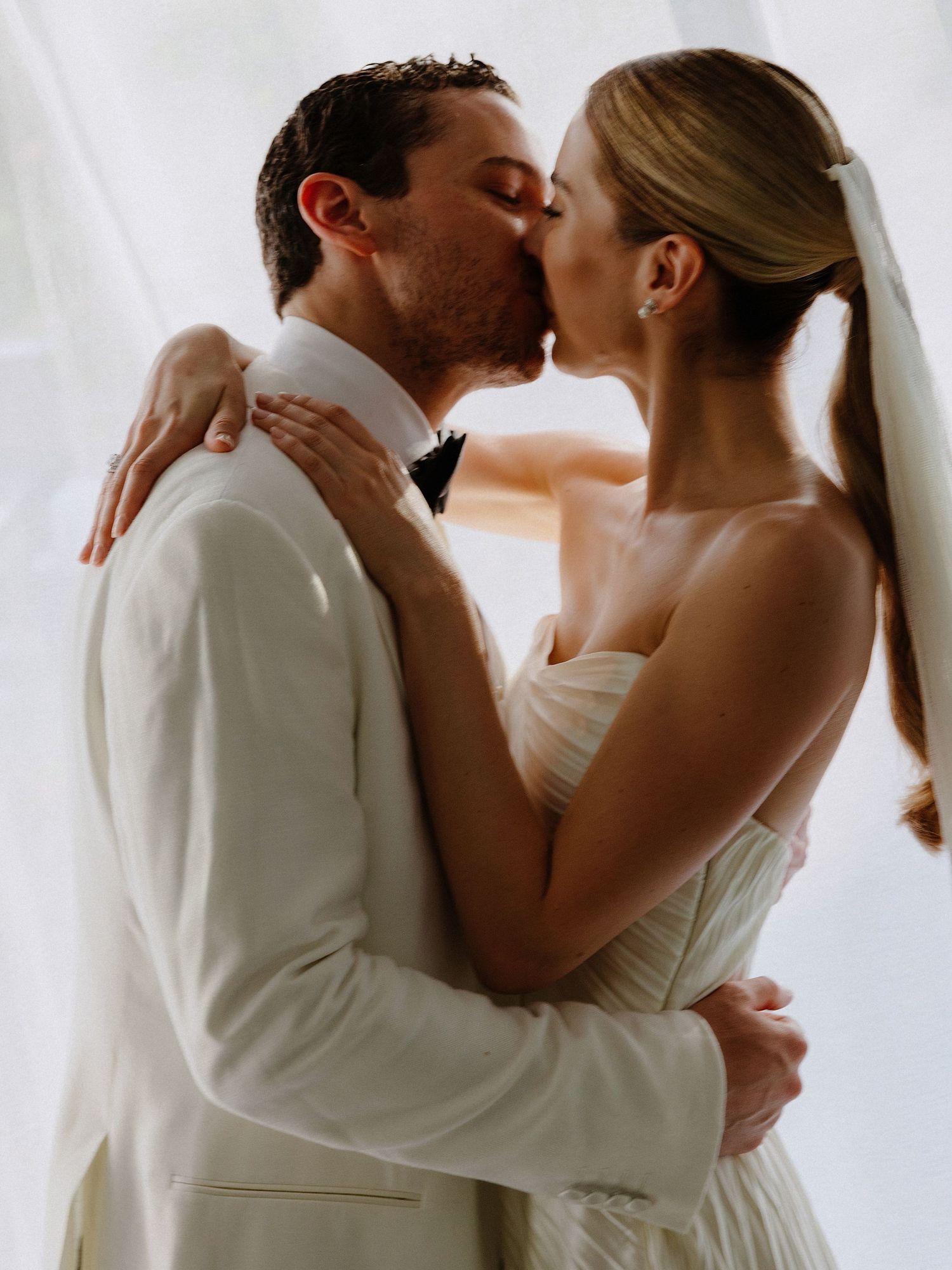 A romantic moment captured between newlyweds sharing their first kiss in elegant wedding attire.