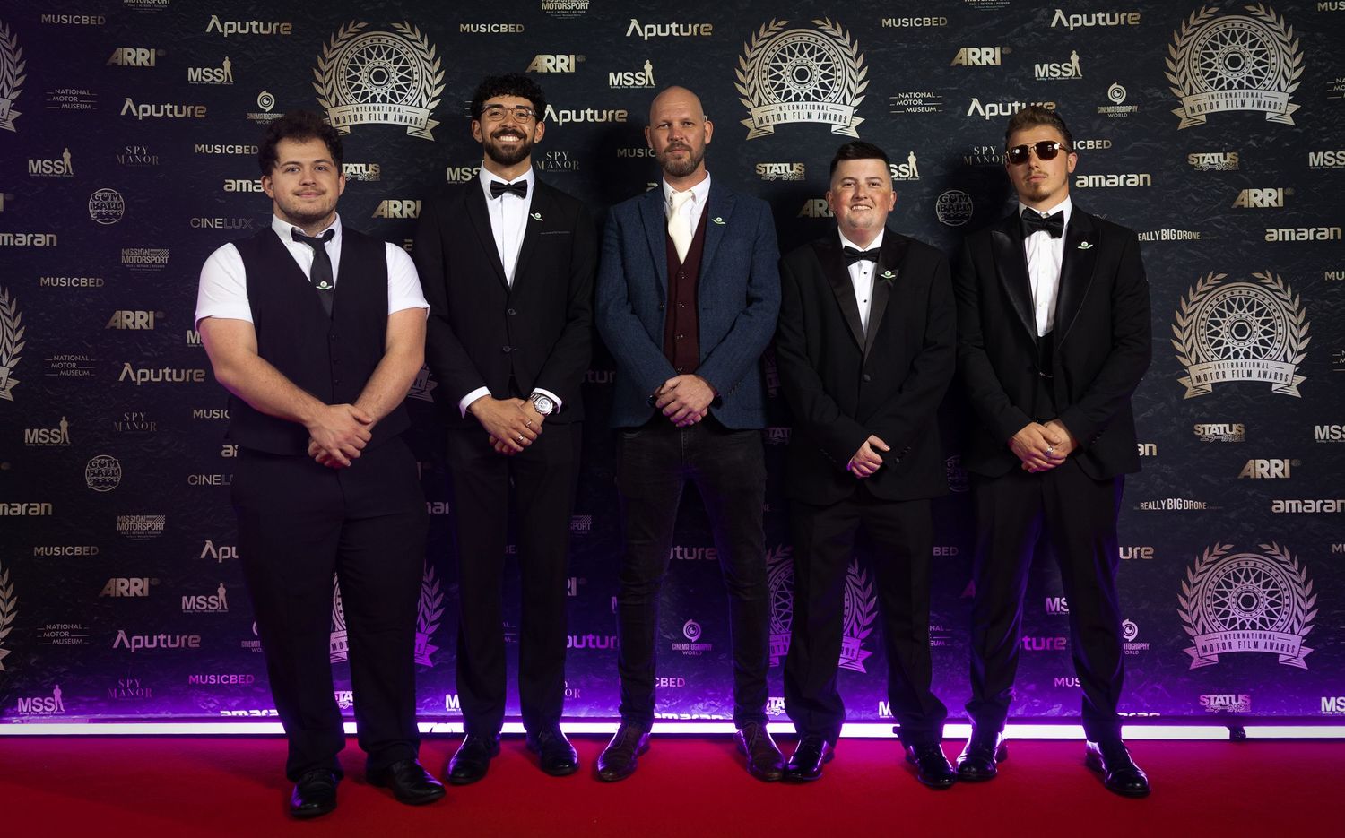 A group of formally dressed people pose together on a red carpet at an awards ceremony or gala event.