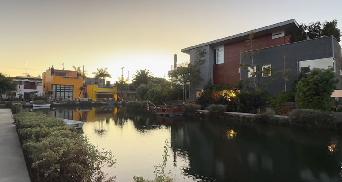 Colorful houseboats and floating homes line a peaceful canal at sunset in a waterfront community.