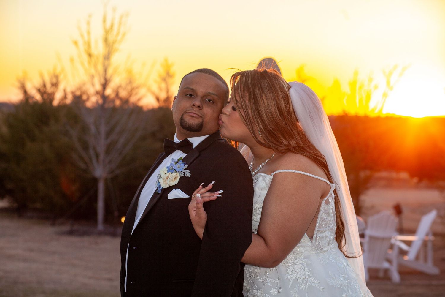 Couple embraces during golden sunset at outdoor wedding ceremony with orange sky in background.