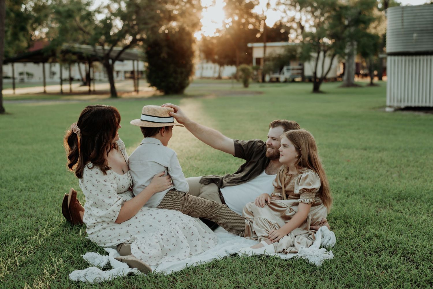 Family members hold hands in a circle during an outdoor gathering in a grassy gladstone field at sunset.