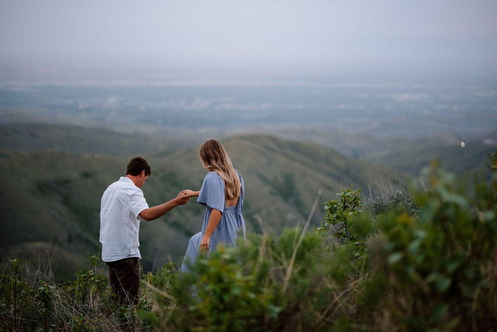 A couple shares a special moment on a scenic hilltop overlooking misty mountain valleys at dusk.