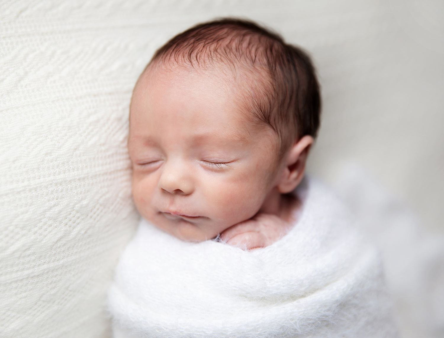 Peaceful newborn sleeps while wrapped snugly in soft white blankets creating a serene portrait. During a newborn session in Bexley