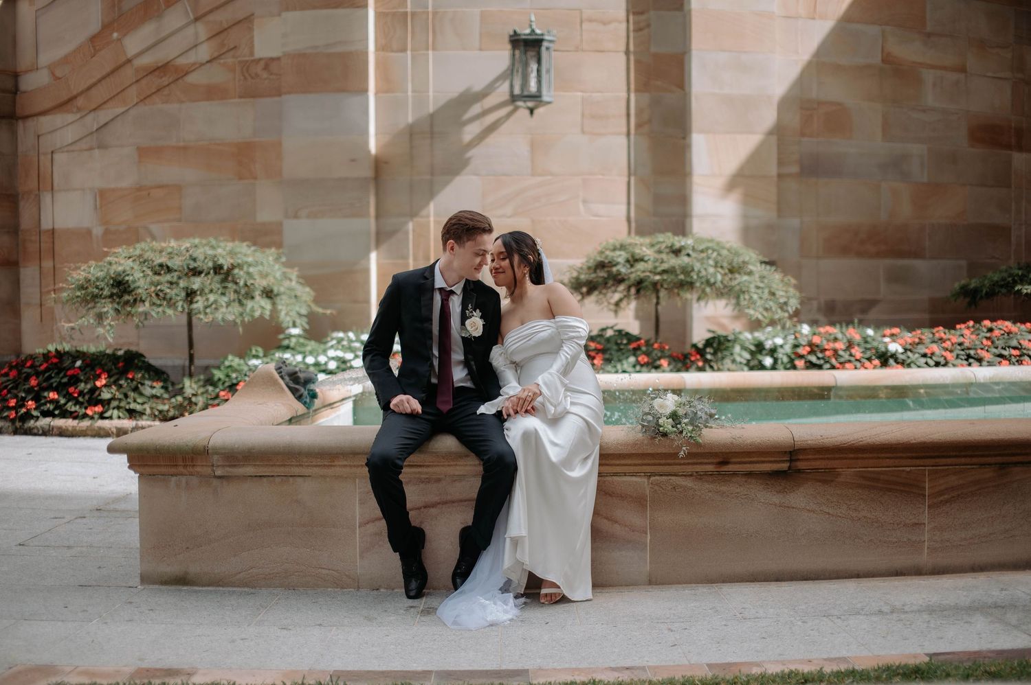A romantic couple in formal attire poses together on stone steps at an elegant outdoor venue.