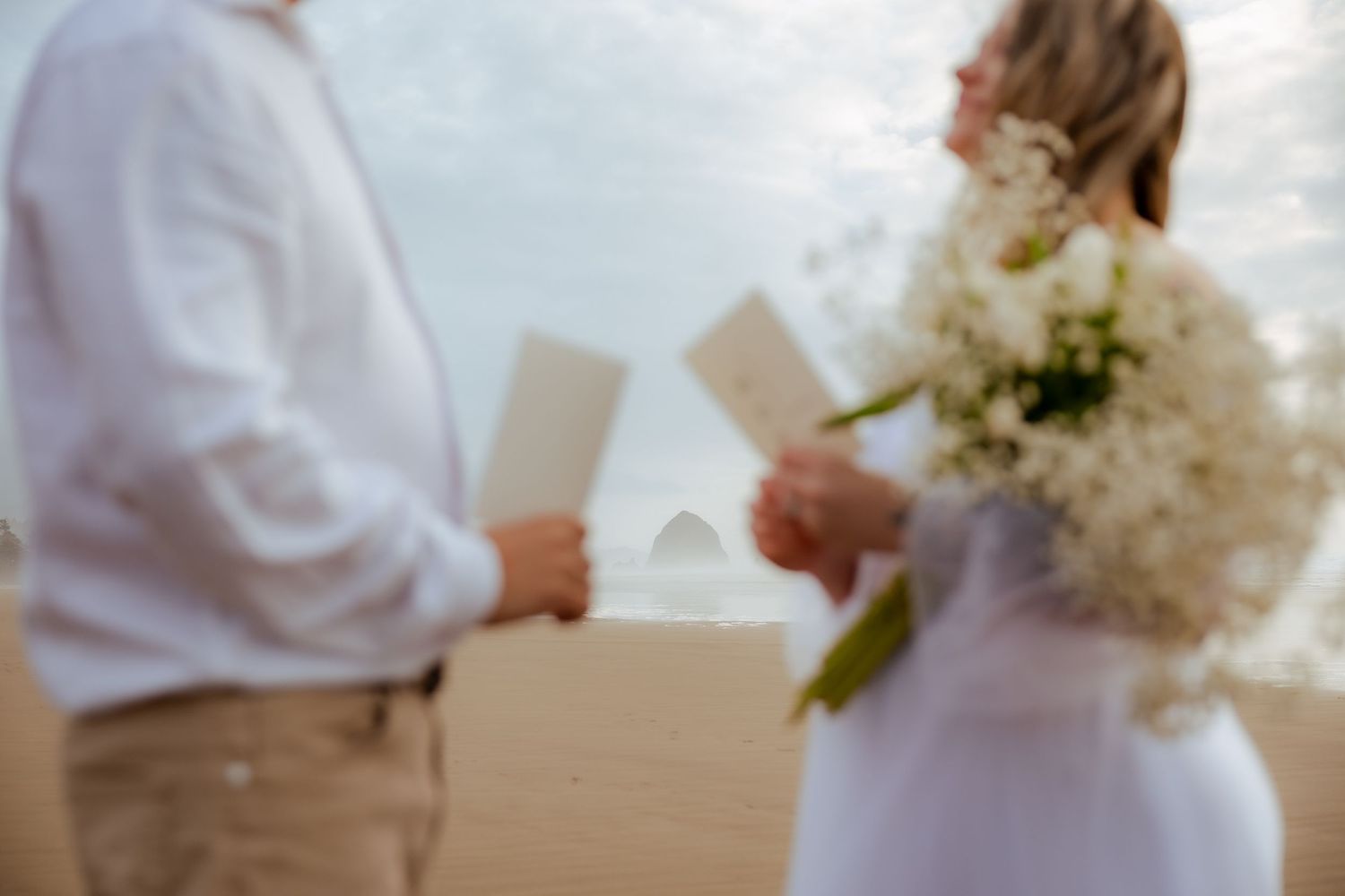 Couple walking along coastal grass path with cloudy sky backdrop.