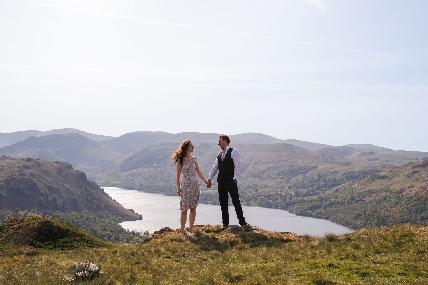 Couple stands together on a cliffside overlooking a scenic mountain lake and valley on a misty afternoon.
