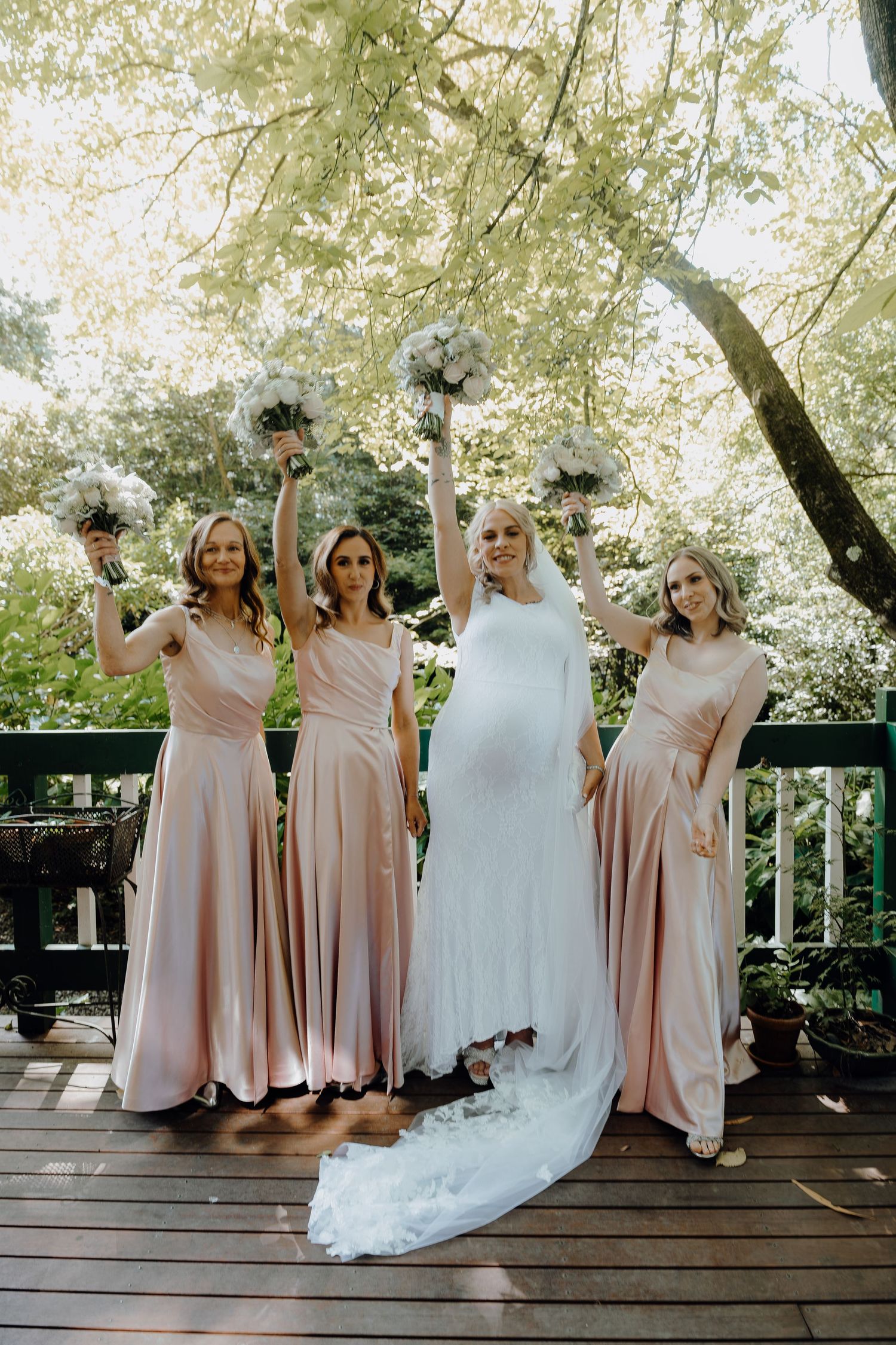 Four women in matching sage green dresses dance and pose playfully on a white carpet in a bright room.