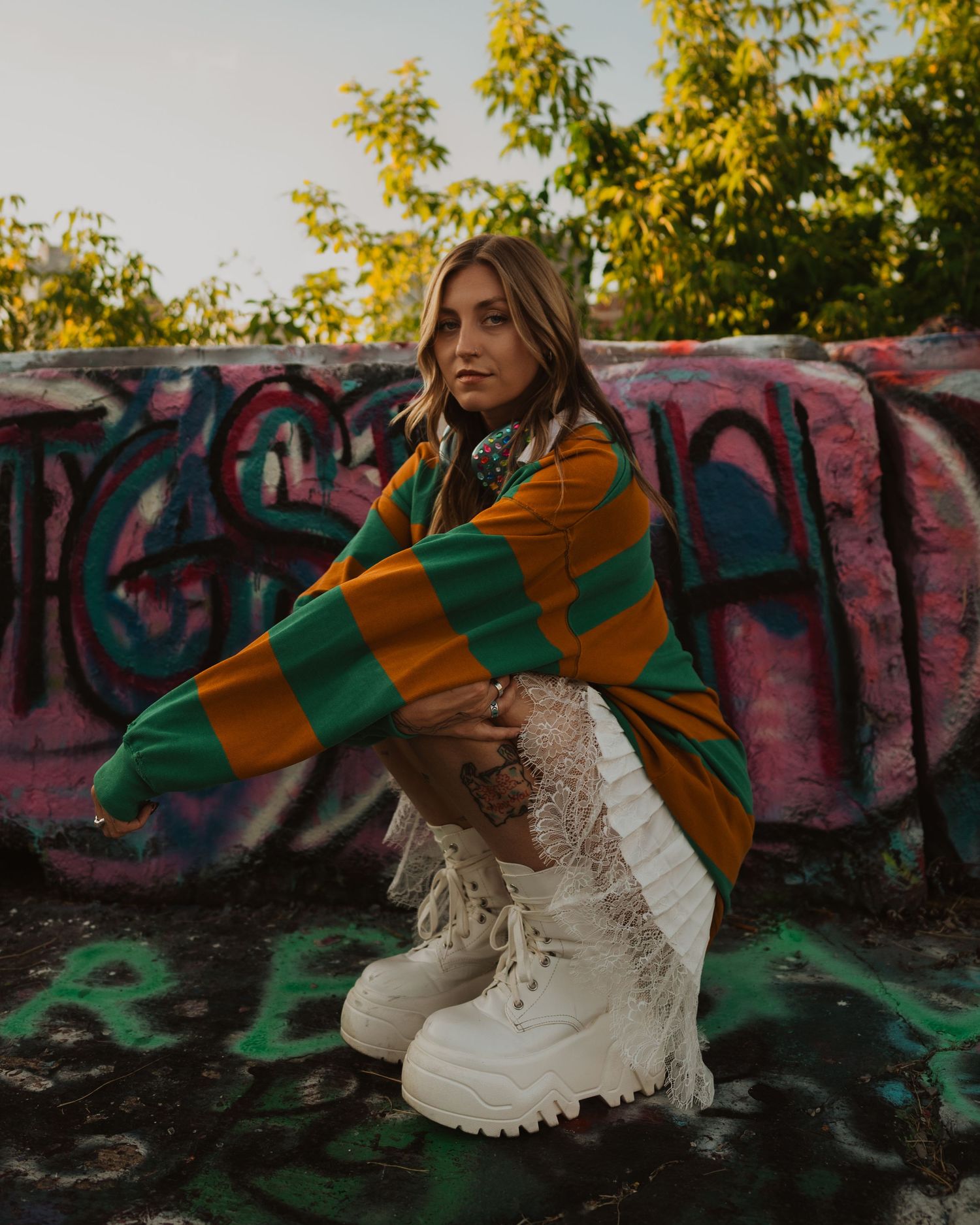 Casual autumn fashion with striped orange and green sweater paired with white boots against graffiti wall background.