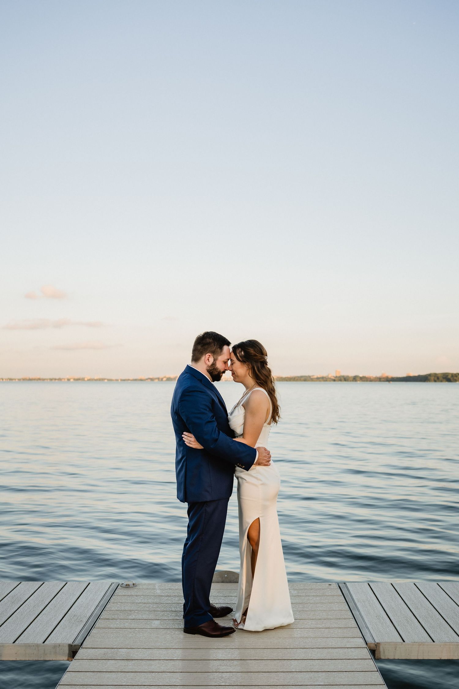 TJ + Ashley stand face-to-face in front of Lake Monona at sunset.