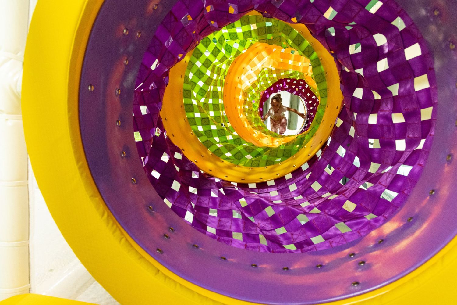 Abstract circular pattern with yellow and purple swirls creates a spiraling psychedelic tunnel effect.