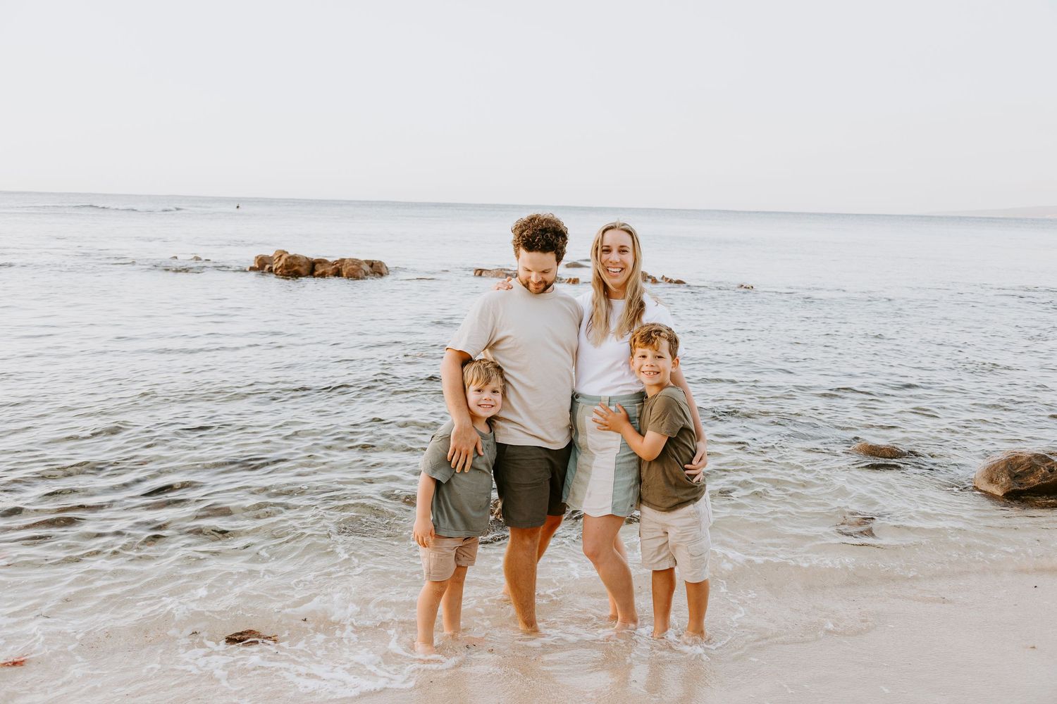 A joyful family plays and splashes together in the shallow ocean water at sunset.