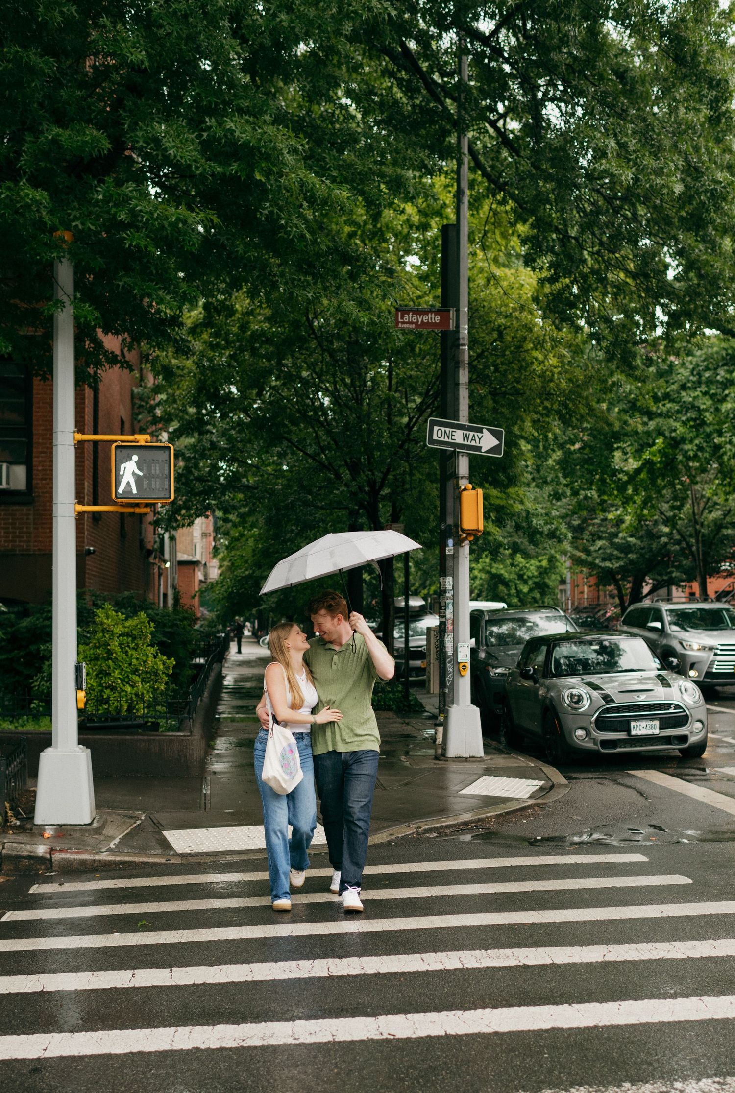 A couple sharing an umbrella while walking across a wet city crosswalk.