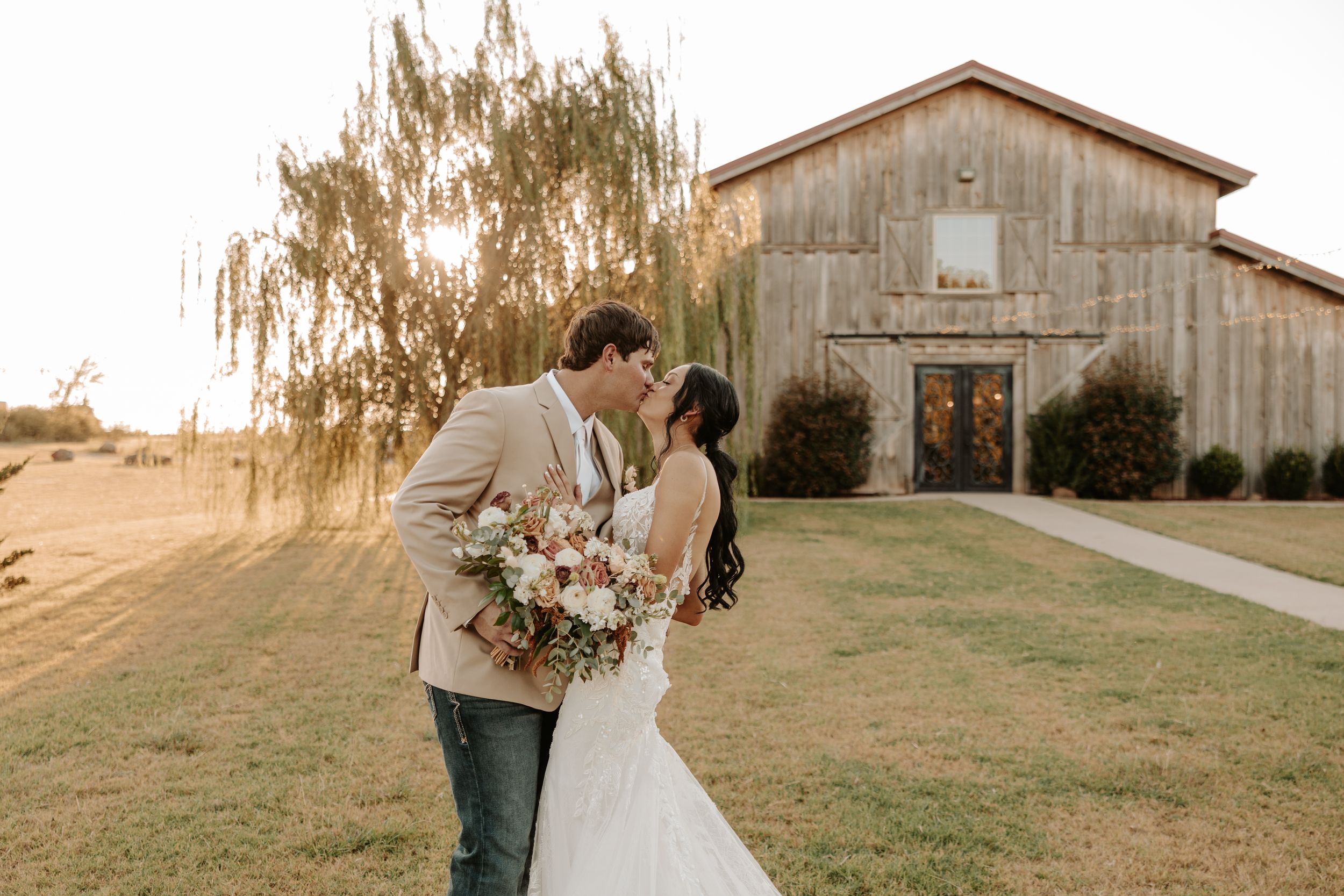 A romantic couple shares tender moments in front of a rustic barn during a golden sunset wedding photoshoot.