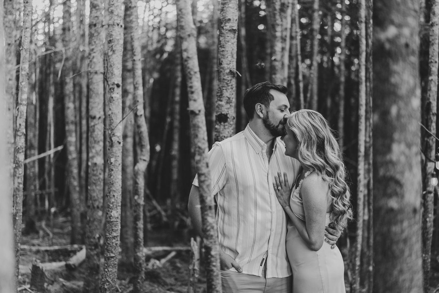 Two people laugh and embrace during a romantic engagement photo session in a misty evergreen forest.