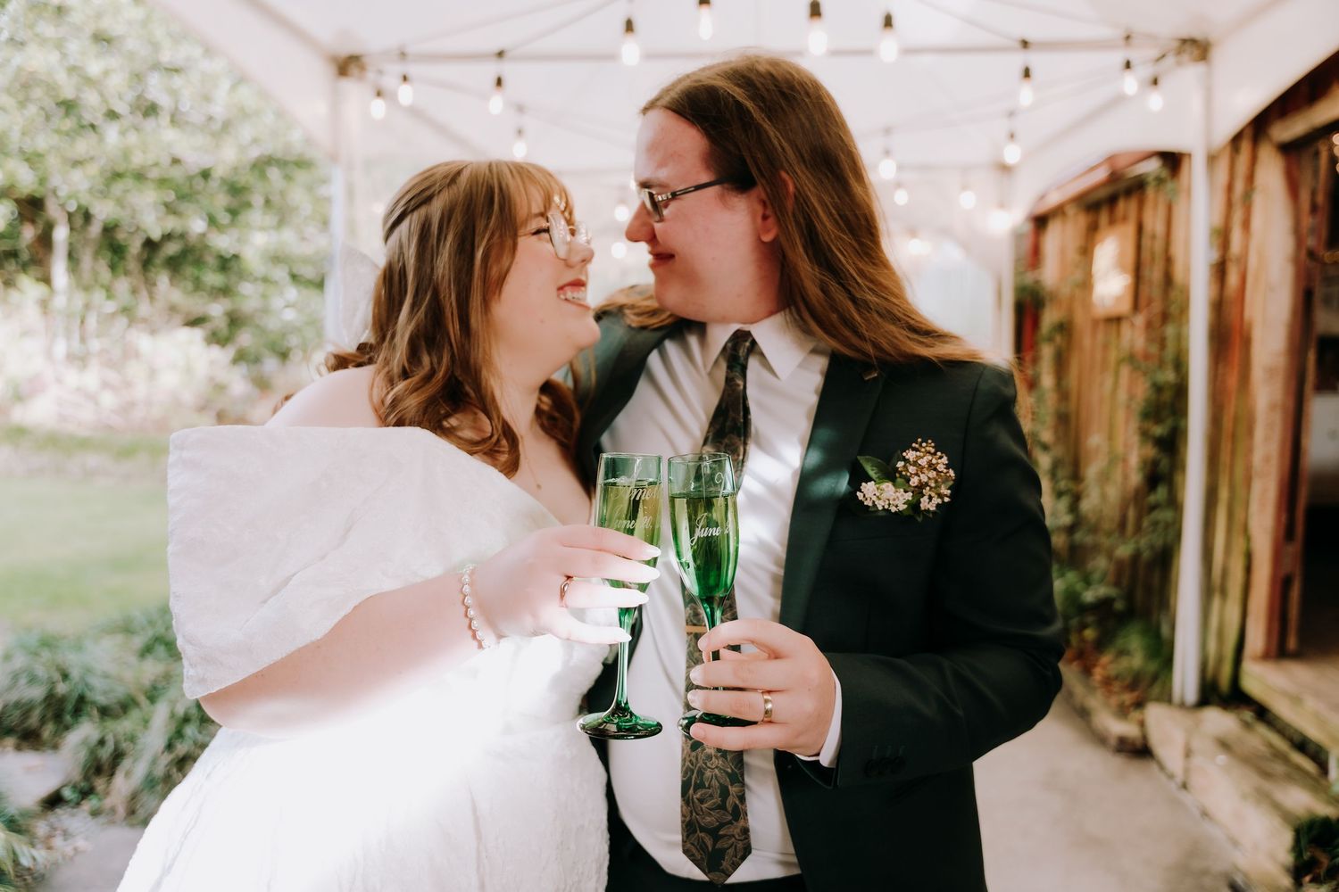 Two people share a joyful moment with champagne glasses on a rustic patio decorated with string lights.