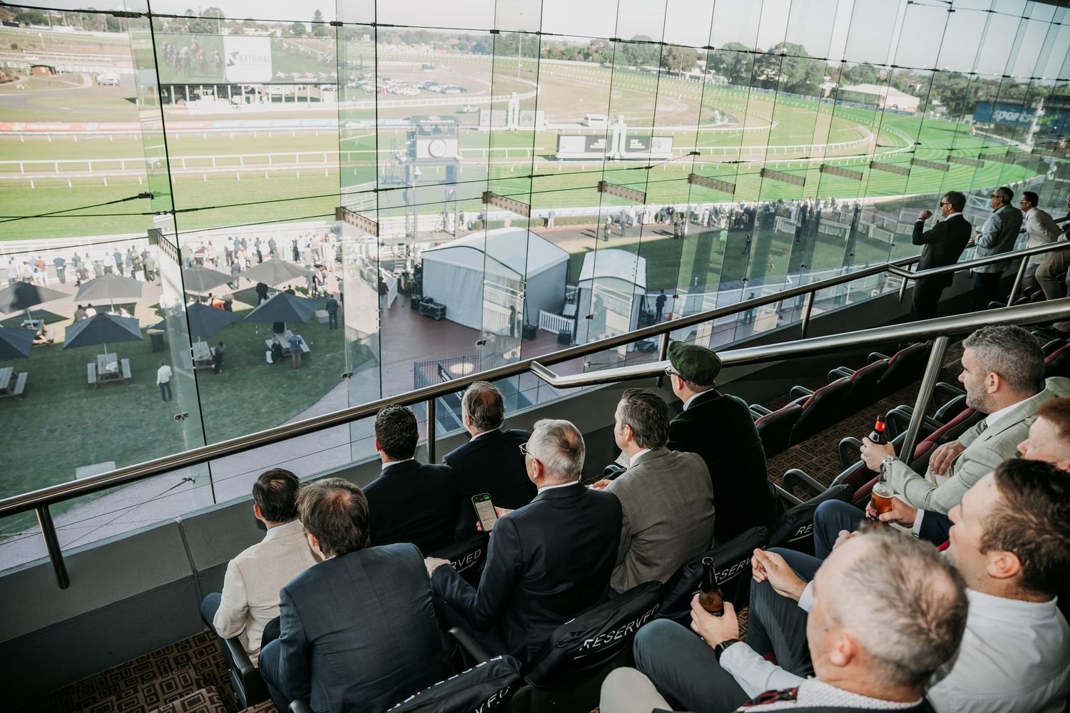 Spectators watching an event from behind glass windows in a viewing area or press box.