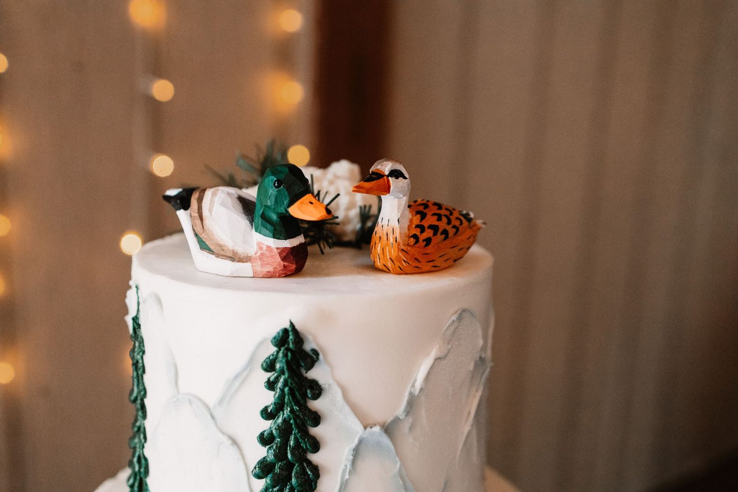 White wedding cake topped with duck and bird figurines with pine tree details.