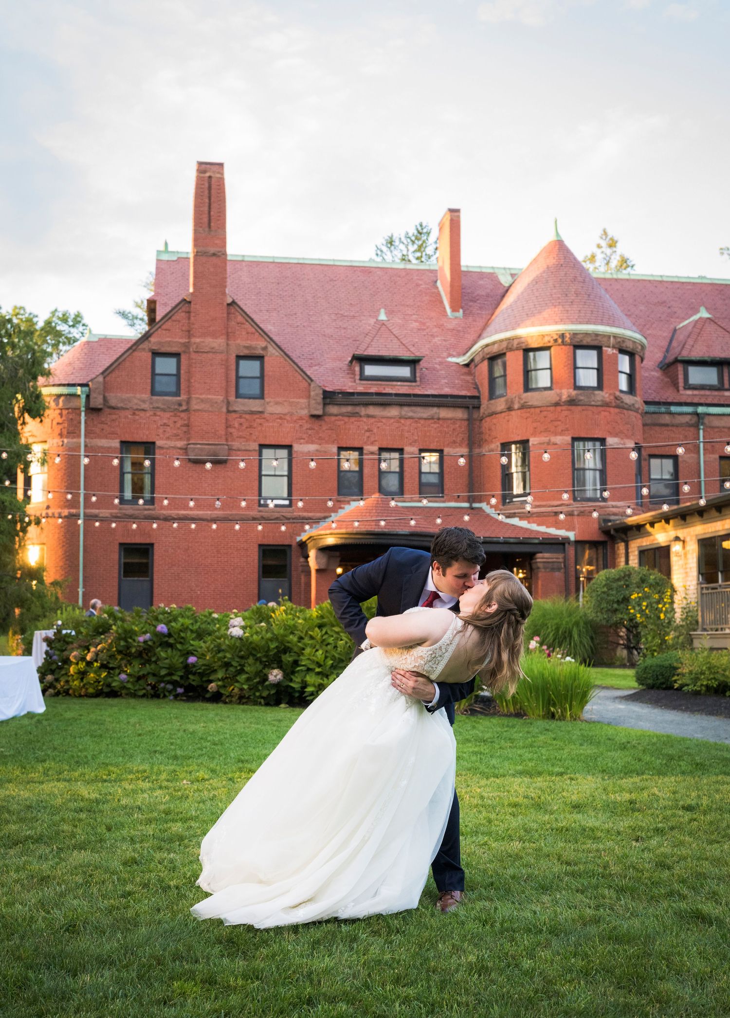 A couple share clear umbrellas on their rainy wedding day in front of a Victorian garden gazebo.