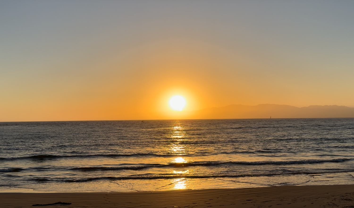 Golden sunset over calm ocean waves on a sandy beach with vibrant orange sky reflecting on the water.