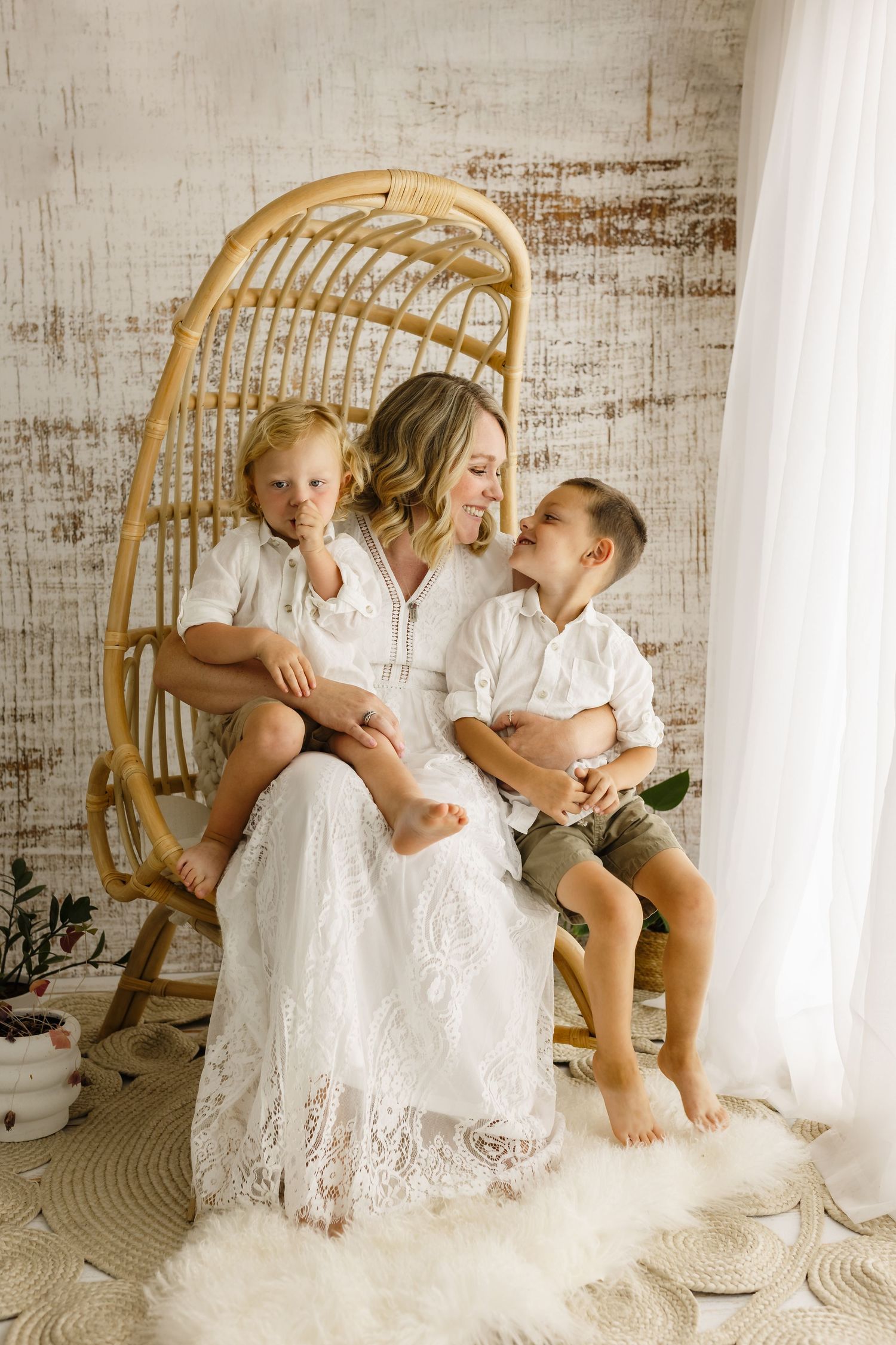 Mother in white gown holds her boys against a warm white backdrop during a mommy and me session by Charlottesville family photographer.