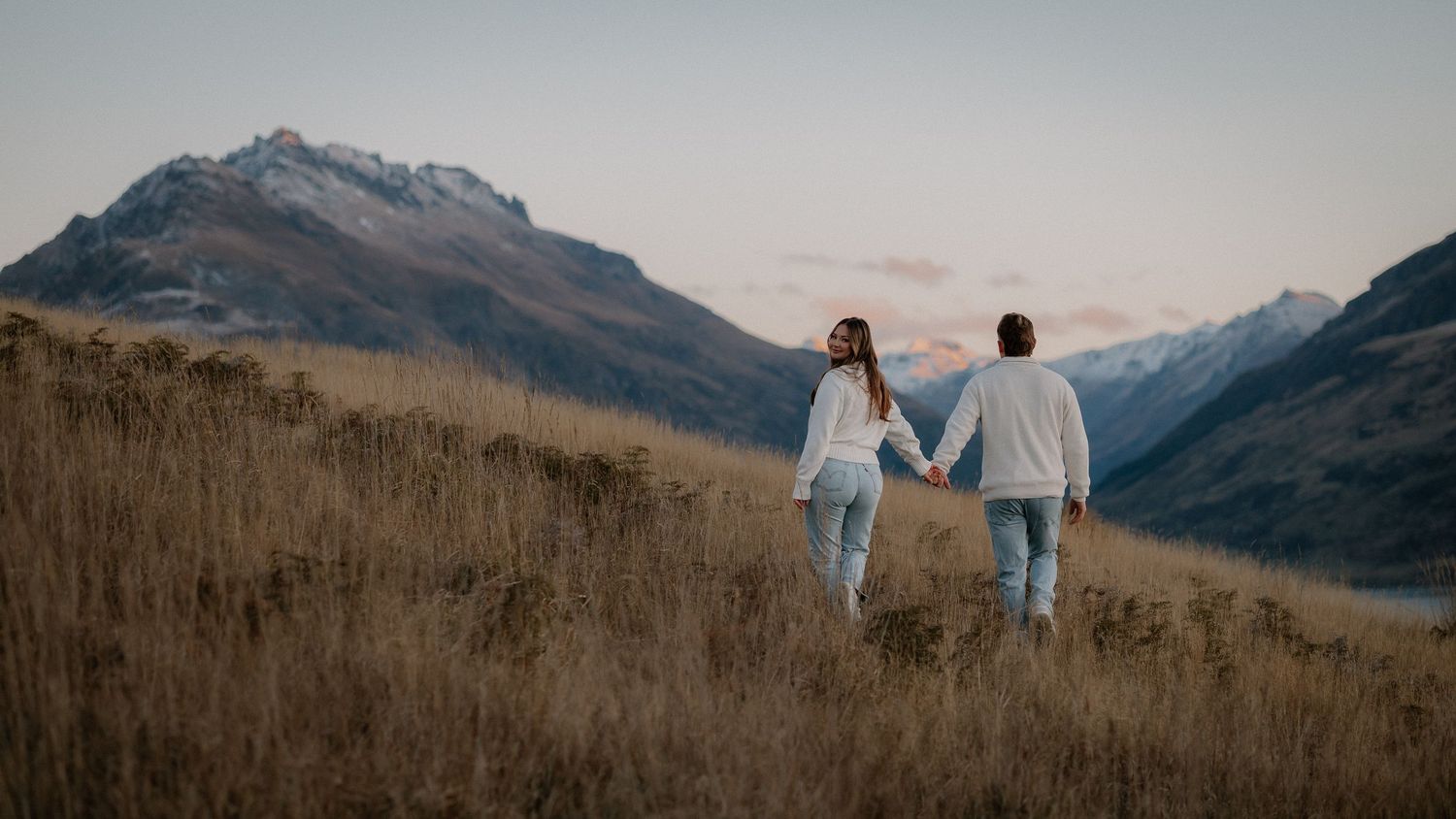 Silhouette of couple embracing in golden wheat field at sunset with mountains in background.