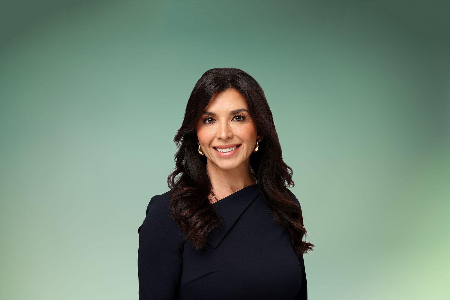 Professional headshot of a smiling woman with dark hair wearing a black blazer against a green background.