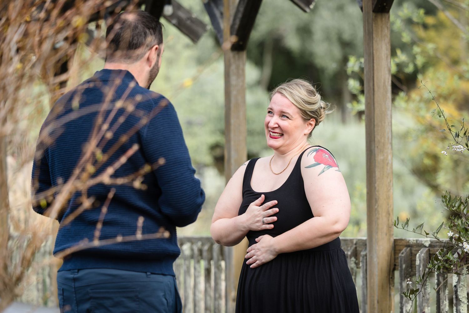 A couple in formal attire shares a romantic moment together in a wooded outdoor setting.