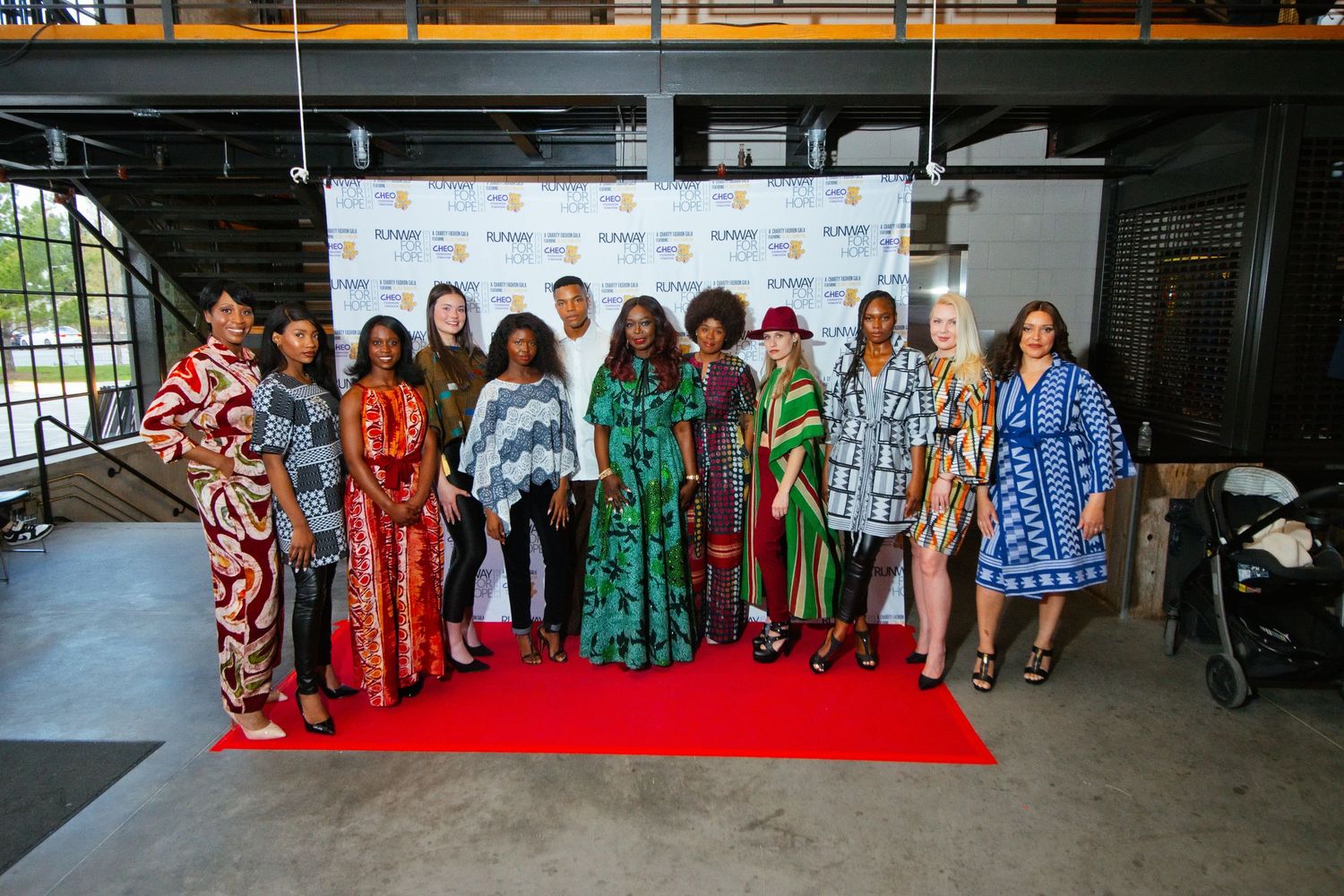 Group of models and House of Grace fashion designer Temilade in vibrant African print outfits posing on red carpet at fashion event.