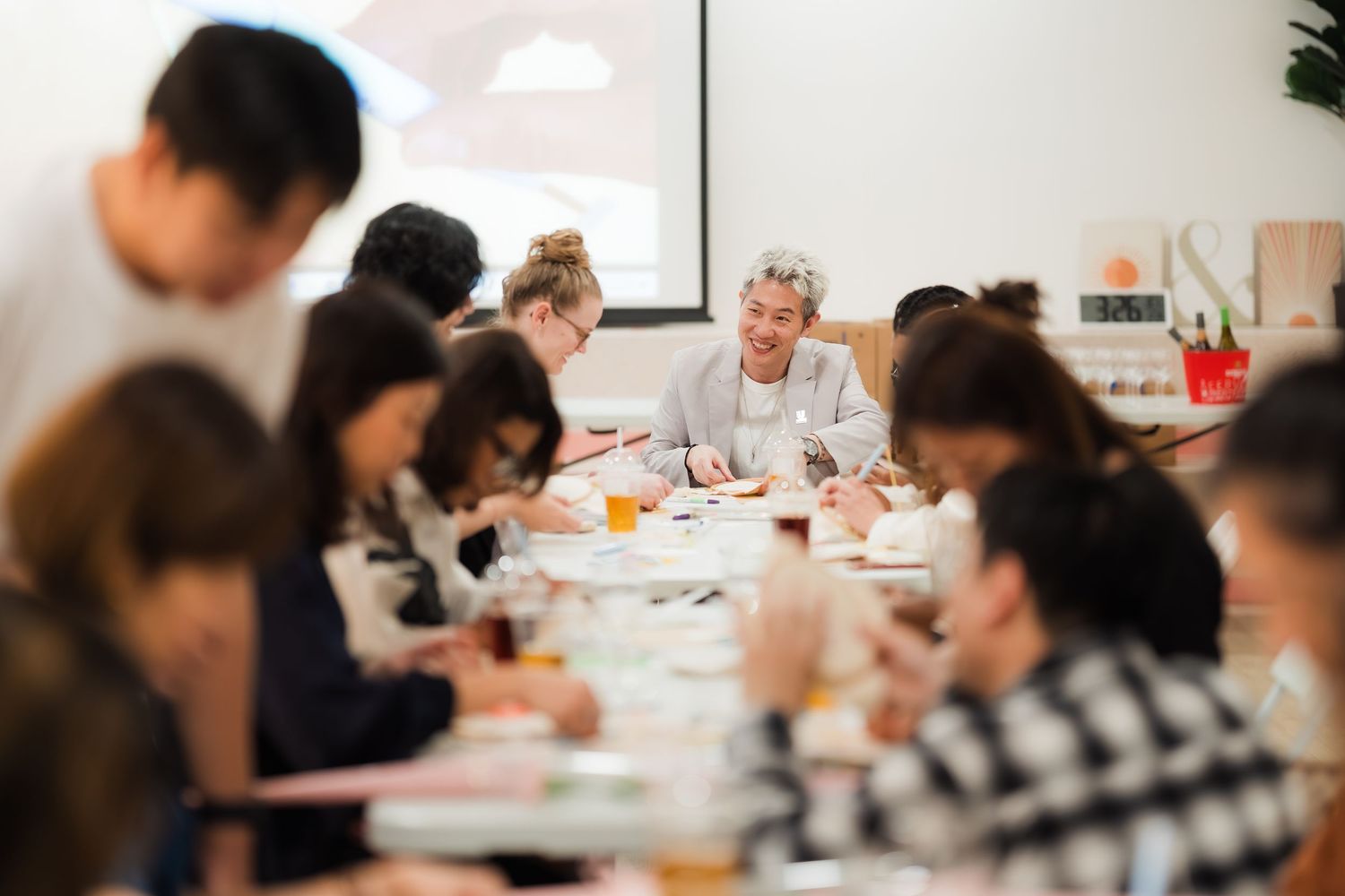 Group of people engaged in a creative workshop, writing and drawing at long tables in a bright studio.