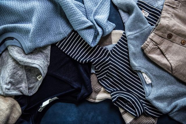 Flat lay of folded blue and striped casual clothing items arranged on a dark surface.