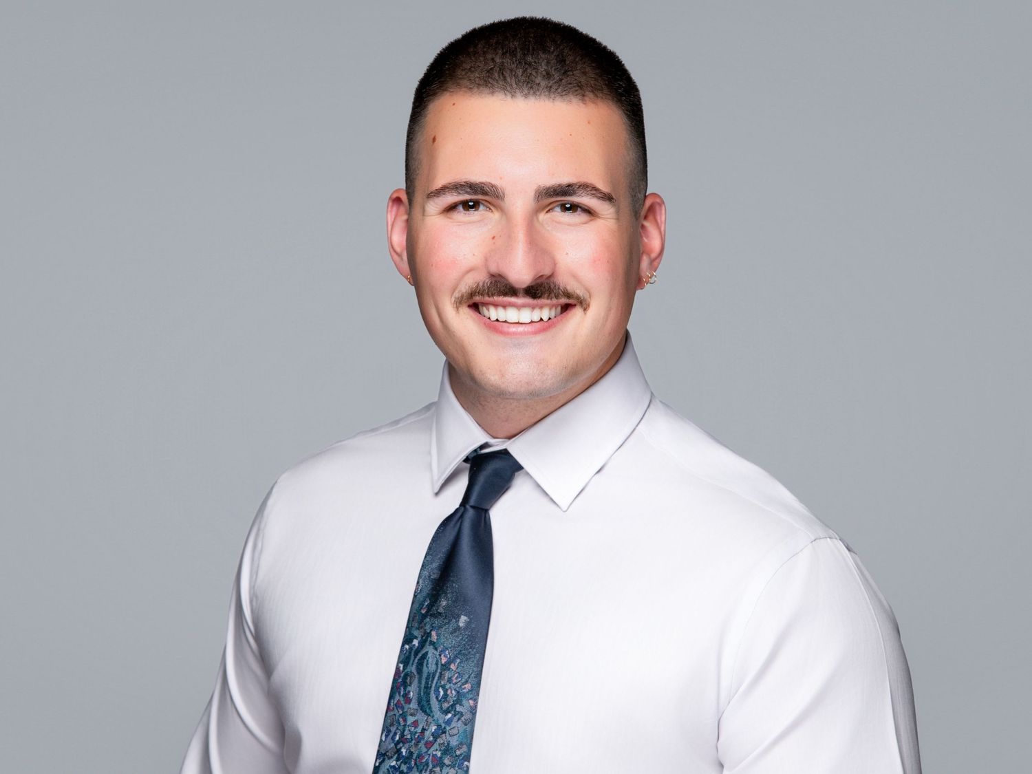 Professional headshot photos of someone wearing a white dress shirt and blue tie against a light gray background.